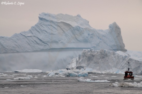 Barco pesquero ante un enorme iceberg